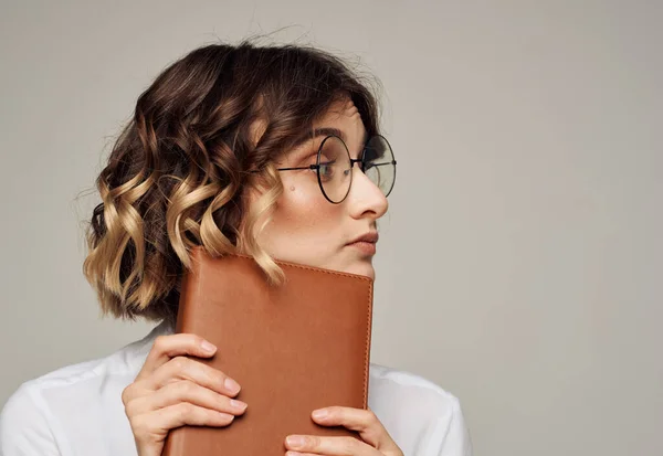 Ρομαντικό γυναίκα με γυαλιά σε γκρι φόντο με ένα καφέ βιβλίο στα χέρια της — Φωτογραφία Αρχείου