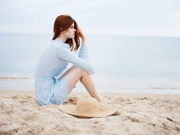 Ρομαντικό γυναίκα κάθεται με καπέλο και μπλε φόρεμα άμμο θάλασσα — Φωτογραφία Αρχείου