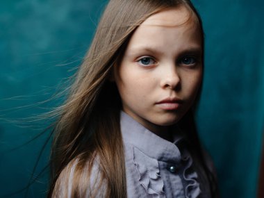 Turkuaz arka planda gri elbiseli bir kızın portresi gevşek saçlarının yakın plan çekimi.