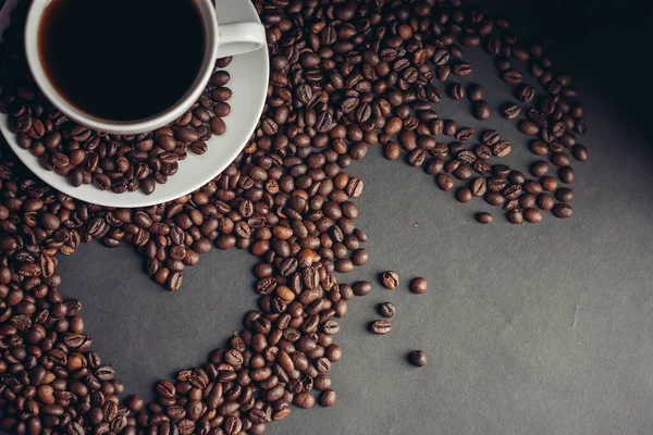 Corazón extraído de granos de café y una taza con un desayuno platillo bebida en la cama — Foto de Stock