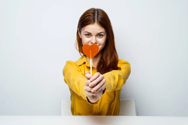 Sarı tişörtlü, elinde kalp şeklinde lolipop olan güzel bir kadın. — Stok fotoğraf