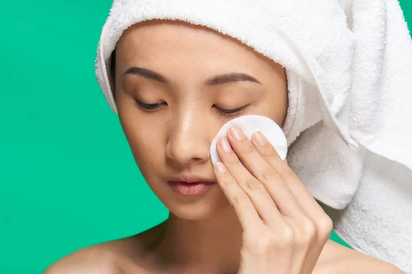 女人用棉垫擦拭她的脸，裸露的肩膀干净的皮肤绿色背景 — 图库照片