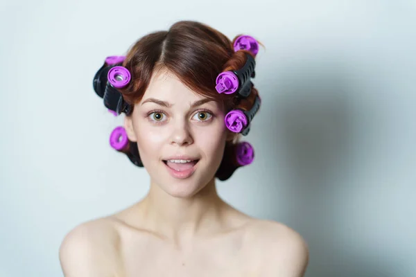 Young woman with purple curlers on her head naked shoulders gray background — Stock Photo, Image