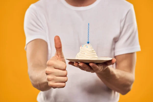 Un hombre con un pastel de cumpleaños en sus manos sobre un postre de cumpleaños de fondo amarillo — Foto de Stock