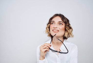 Kısa saçlı ve beyaz gömlekli bir kadın ellerinde gözlük tutuyor.