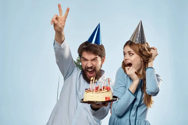 Uomo e donna festeggiano il compleanno con torta e cappelli su sfondo blu — Foto Stock