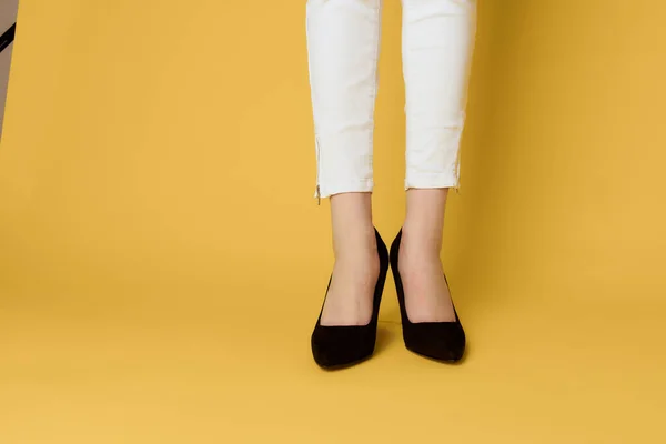 Piernas femeninas zapatos negros moda atractivo look blanco jeans fondo amarillo — Foto de Stock