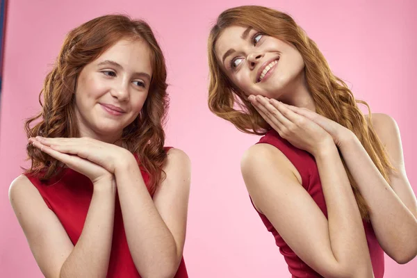 Mutter und Tochter in roten Kleidern umarmt Spaß Fratze Kindheit Freude rosa Hintergrund — Stockfoto