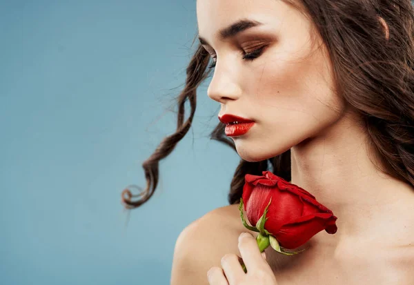 Femme avec une fleur rouge près du visage sur un fond bleu épaules nues ombres sur les paupières — Photo