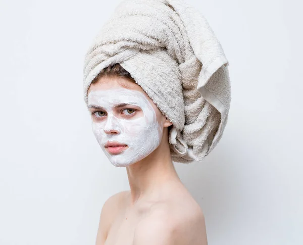 Ładna kobieta pielęgnując białą maskę twarzy i ręcznik na głowie — Zdjęcie stockowe