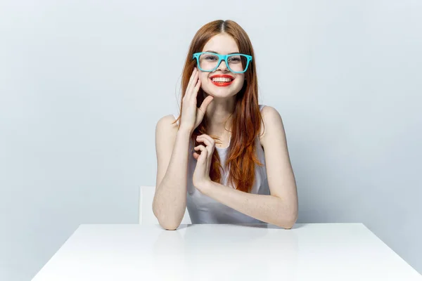 Mooie roodharige vrouw zitten aan de tafel met een blauwe bril rode lippen — Stockfoto