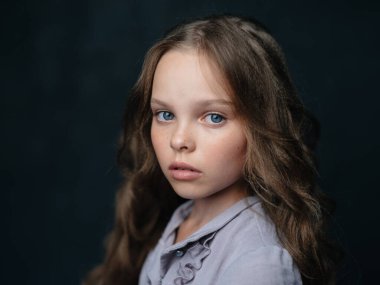 Mavi gözlü bir kızın portresi koyu gri bir elbisenin arka planında ve kırpık manzaralı.