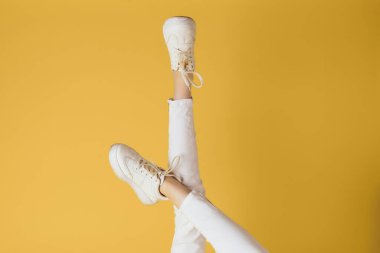 Kadınların bacakları, beyaz pantolonlar, şık kıyafetler, sokak tarzı sarı arka plan.