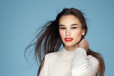 Beyaz kazaklı esmer, kırmızı dudaklı, uzun saçlı, mavi arkaplan.