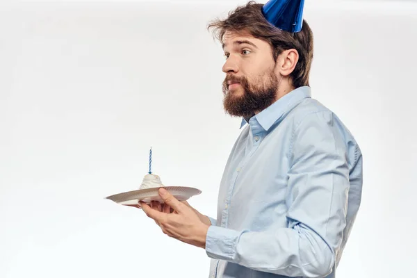 Um homem comemora um aniversário em um fundo leve com um bolo em um boné divertido flauta placa — Fotografia de Stock