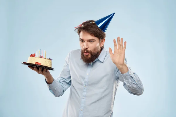 Человек с тарелкой торта и праздничной корпоративной вечеринкой с голубыми свечами на заднем плане — стоковое фото