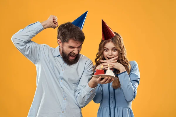 Fiesta de cumpleaños hombre y mujer sobre un fondo amarillo en sombreros con un pastel en sus manos —  Fotos de Stock