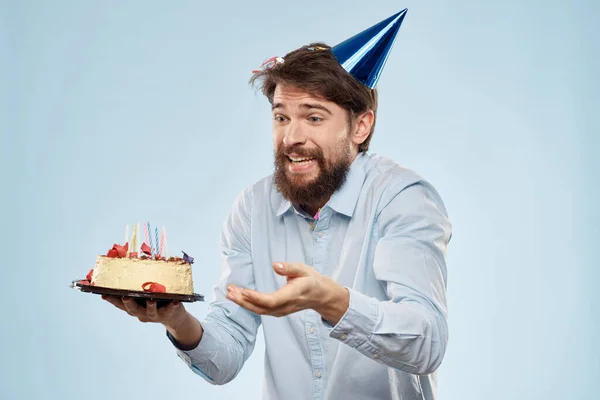 ケーキのプレートとお祝いのキャンドルブルーの背景キャップ企業パーティーを持つ男 — ストック写真