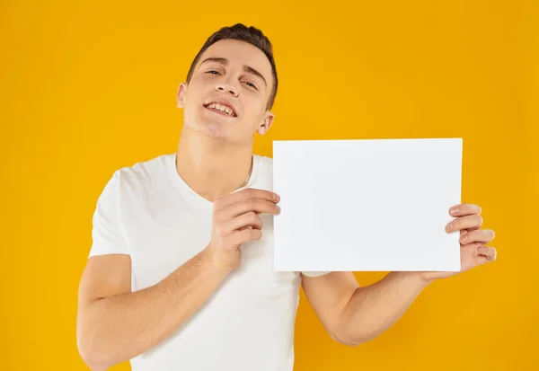 Een man op een gele achtergrond met een mockup in zijn hand een wit vel papier — Stockfoto