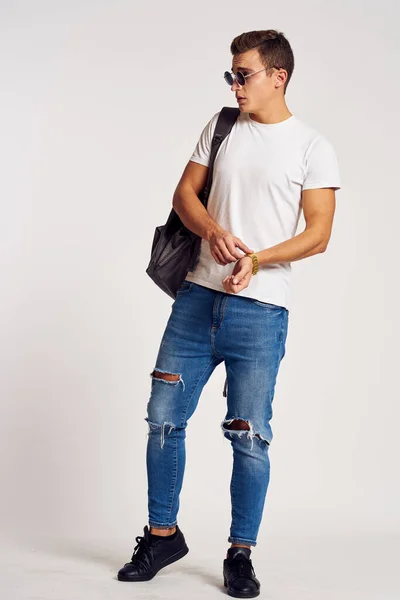 Un hombre con una mochila en la espalda en pantalones vaqueros zapatillas de deporte de longitud completa y gafas en la cara — Foto de Stock