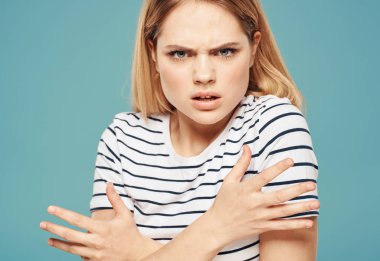 Çizgili tişörtlü bir kadın mavi bir arka plan portresiyle kendine dokunuyor.