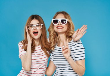 İki güzel kadın elleriyle el kol hareketi yapıyor. Arkadaşlık neşesi yaşam tarzı mavi arka plan.