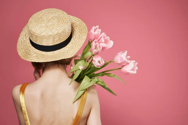 Mulher em um buquê de chapéu de flores em um vestido visão traseira fundo rosa — Fotografia de Stock