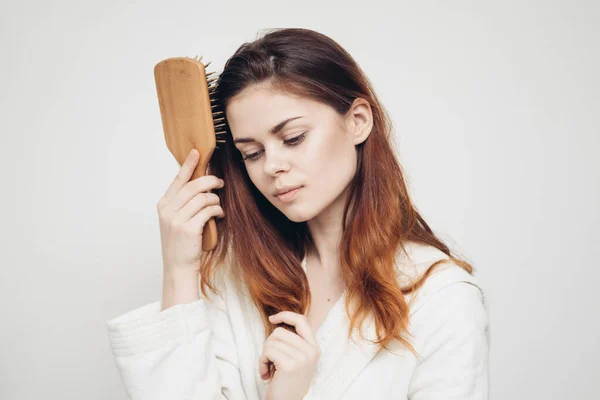 Donna pettinando capelli aggrovigliati e bianco accappatoio luce sfondo ritratto primo piano — Foto Stock