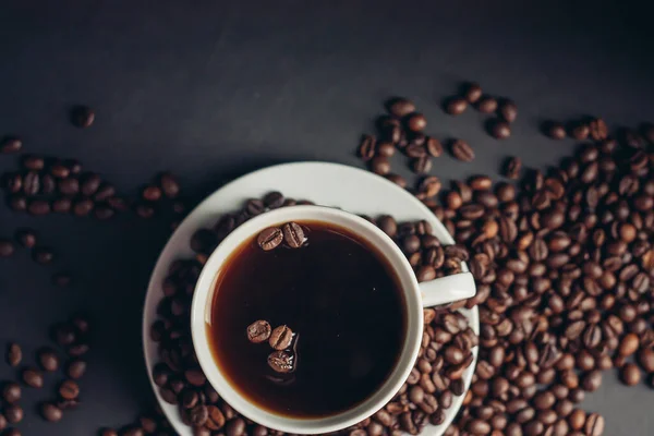 Una taza con una bebida fragante y granos de café alrededor de un platillo vista superior — Foto de Stock