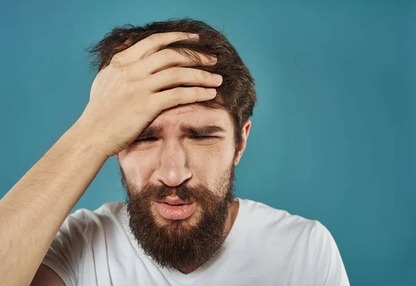 Een man met een blauwe achtergrond raakt zijn hoofd aan met zijn handen. — Stockfoto