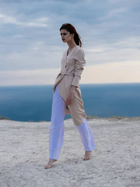 Uma mulher romântica em roupas leves caminha na areia e no oceano ao fundo — Fotografia de Stock