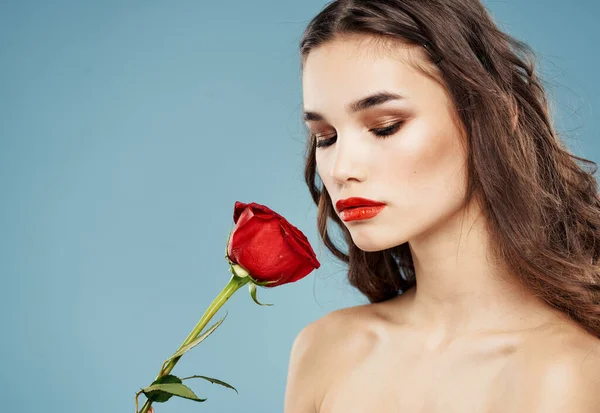 Una donna tiene in mano un fiore rosso su sfondo blu e trucco sul viso — Foto Stock