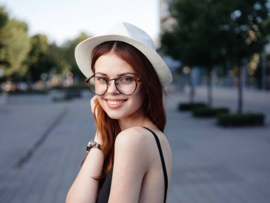 Beyaz şapkalı ve gözlüklü mutlu kadın sokaklarda yürüyor.