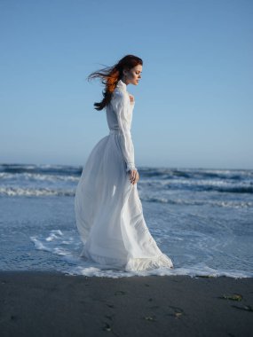 Okyanus kıyısındaki mavi gökyüzü kumsalında uzun elbiseli romantik kadın.