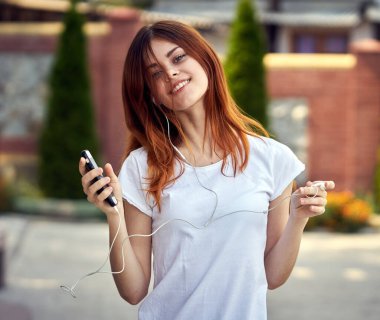 Beyaz tişörtlü bir kadın sokak müziğinde kulaklık takıyor.