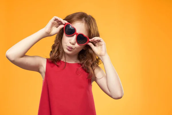 Дівчина в сонцезахисних окулярах у формі серця червона сукня студія жовтого фону дитинства — стокове фото