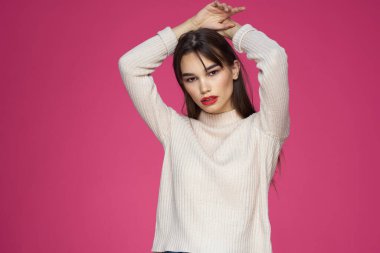 Kırmızı dudaklı, makyajlı beyaz bluzlu, uzun saçlı, pembe arka planlı bir kadın.