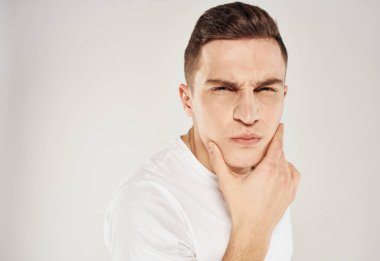 Hafif arka planda bir adam elleriyle yüzüne dokunuyor ve beyaz bir tişört mankeni