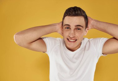 Beyaz tişörtlü enerjik bir adam elini sarı arka planda tutuyor.