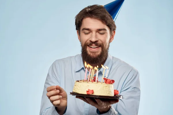 Hombre con un plato de pastel y una vela festiva fondo azul gorra fiesta corporativa — Foto de Stock