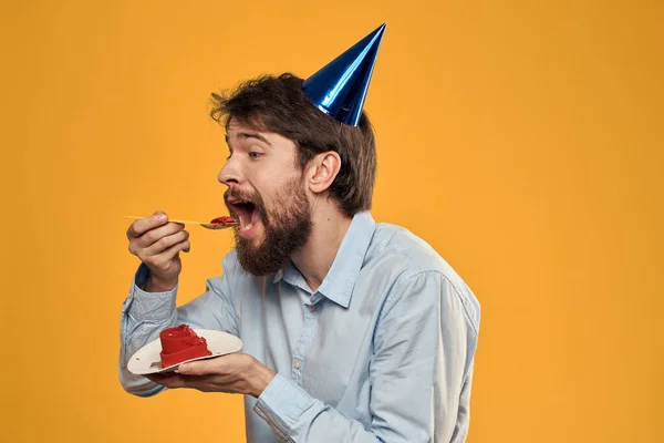 Un homme avec un gâteau d'anniversaire dans les mains et une casquette sur un fond jaune pour son anniversaire — Photo