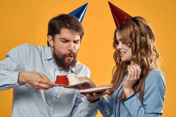 Aniversário festa homem e mulher em um boné com um bolo em um fundo amarelo vista cortada — Fotografia de Stock