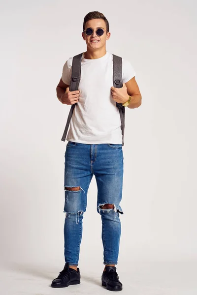 En man med ryggsäck på ryggen i jeans t-shirt full längd sneakers och glasögon på ansiktet — Stockfoto