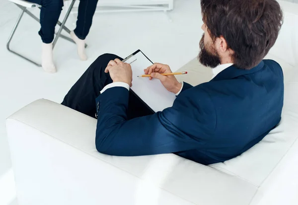 Ein Geschäftsmann im Anzug sitzt auf einem weißen Sofa In einem hellen Raum, Seitenansicht — Stockfoto