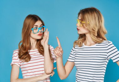 Moda stüdyosunda sosyalleşen iki kız arkadaş mavi arka planda.