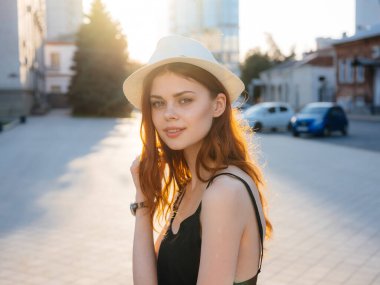 Siyah elbiseli ve beyaz şapkalı bir kadın portresi. Gün batımında binanın yanındaki sokakta.