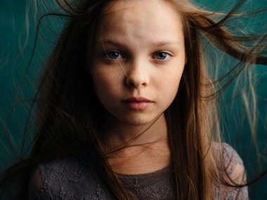 Turkuaz arka planda dağınık saçları olan tatlı küçük bir kız güzel bir yüz.