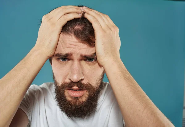 Een man met een blauwe achtergrond raakt zijn hoofd aan met zijn handen. — Stockfoto