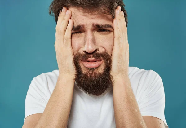 Verontrust man met een baard raakt zijn hoofd met zijn handen op een blauwe achtergrond — Stockfoto