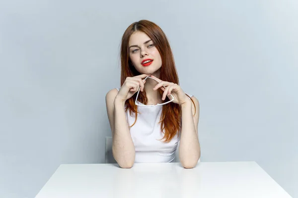 Mulher elegante com lábios vermelhos sentados à mesa óculos nas mãos — Fotografia de Stock